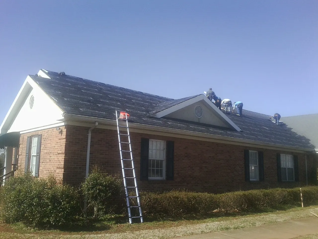 Crew tearing shingles off a brick ranch roof with a ladder set — Emergency Roof Repair work by our crew in American Falls