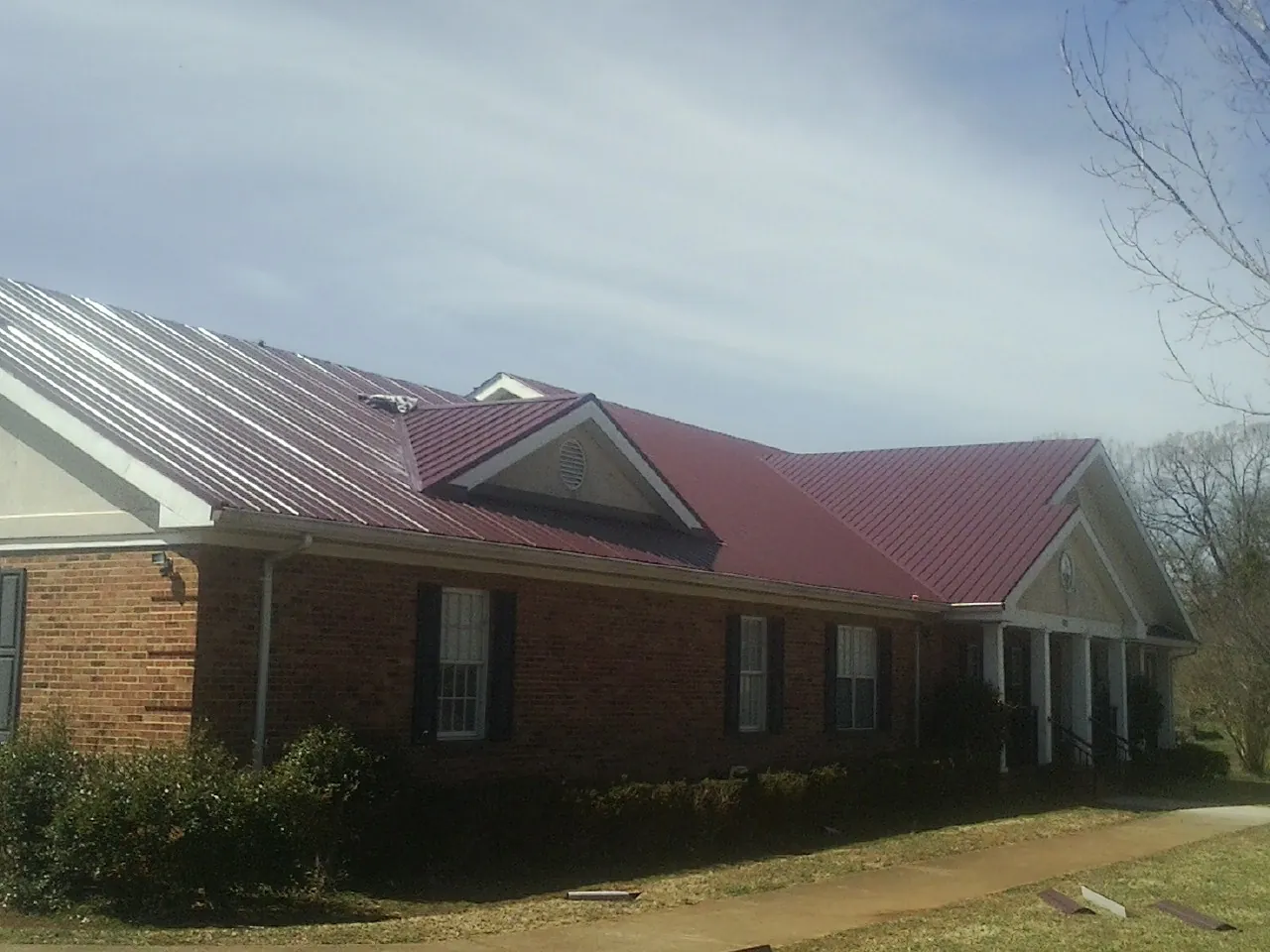 Red metal roof with gabled entries on a long brick building, from a Hail Damage Roof Repair job in American Falls