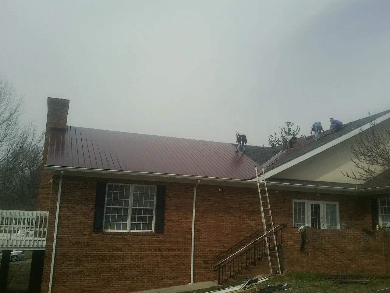 Crew setting red metal roofing panels on a brick home in American Falls