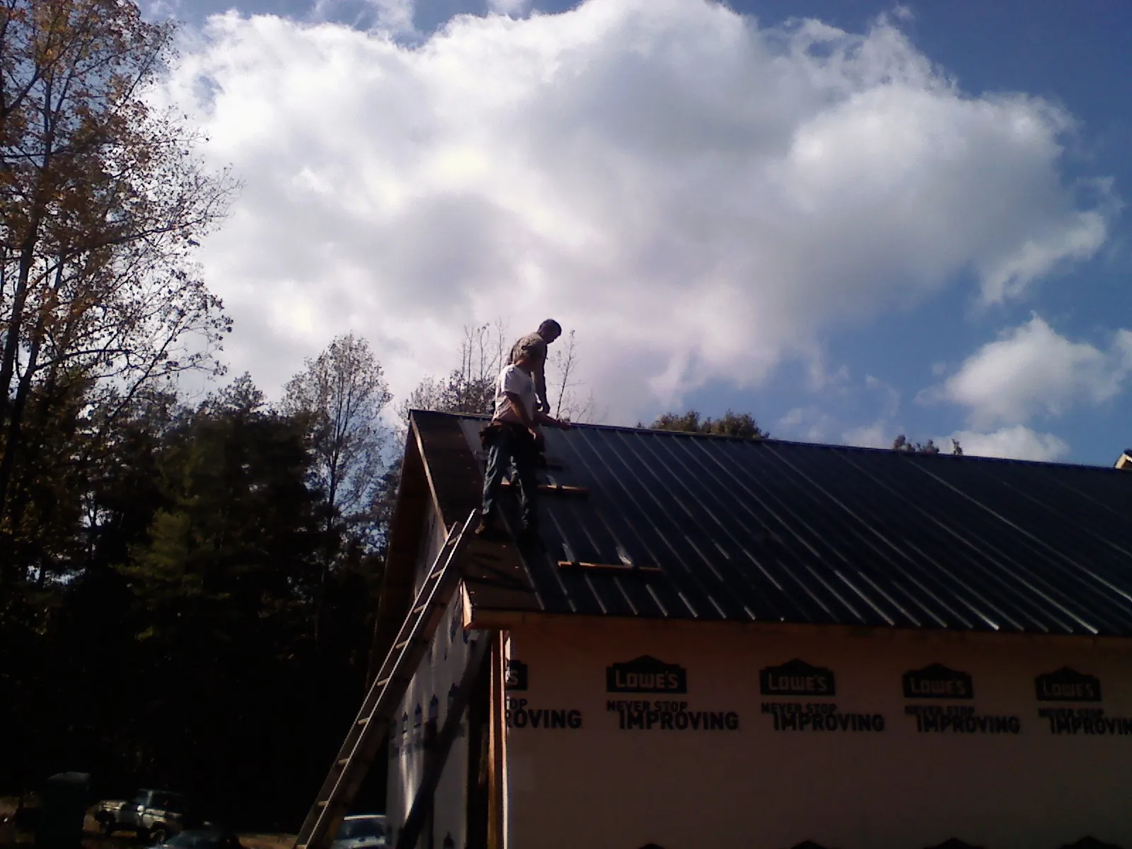 Roofer fastening dark metal panels high against a cloudy sky, from a Roof Inspection job in American Falls