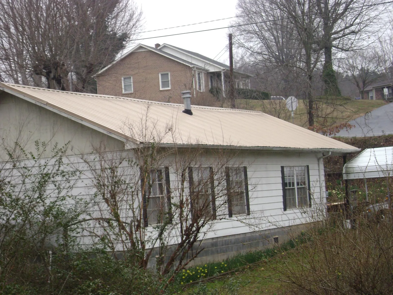 Tan metal roof on a white sided house set into a hillside — Commercial Roofing by Roofing Brothers in American Falls